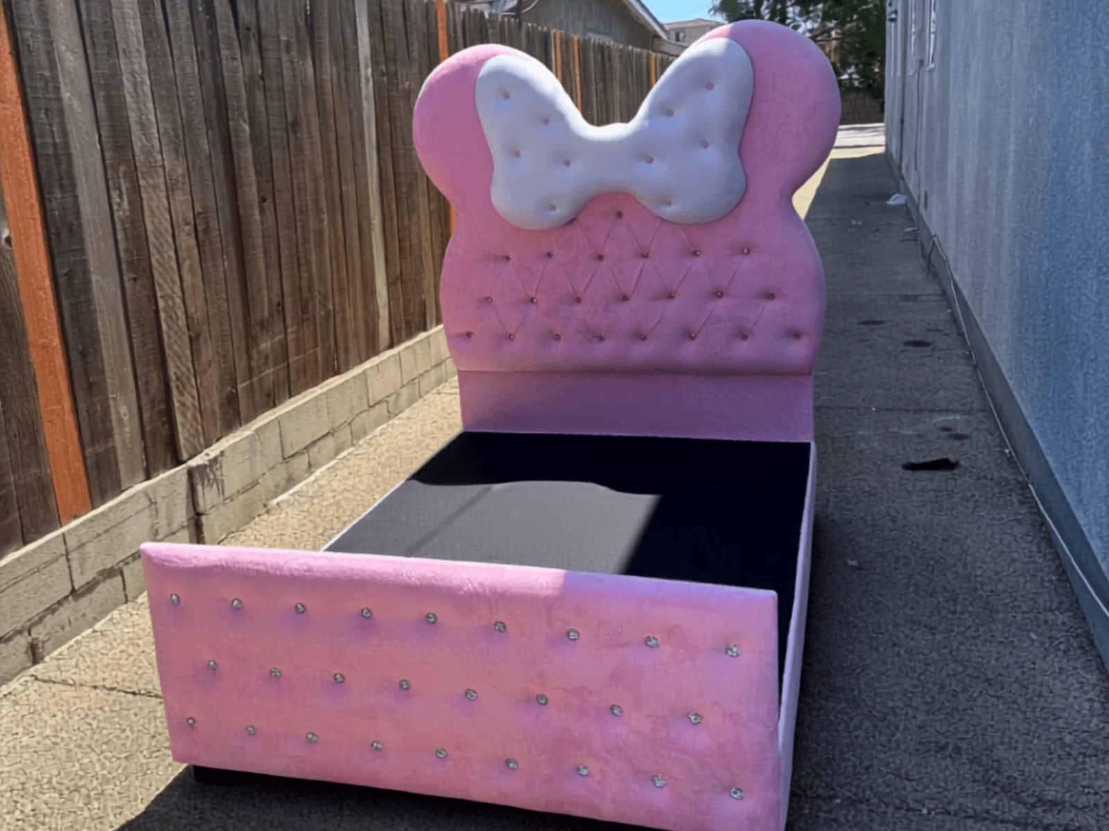 Pink velvet bed with a white bow headboard, diamond tufting and crystal buttons, seen from the foot of the frame