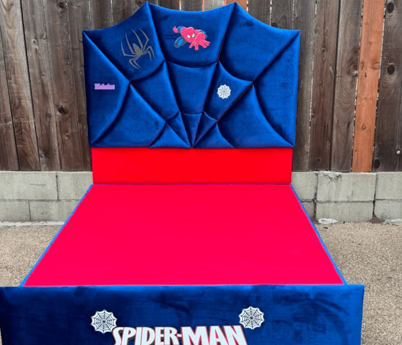Blue pleated web-panelled headboard above a red upholstered platform bed, with a spider motif and an embroidered name