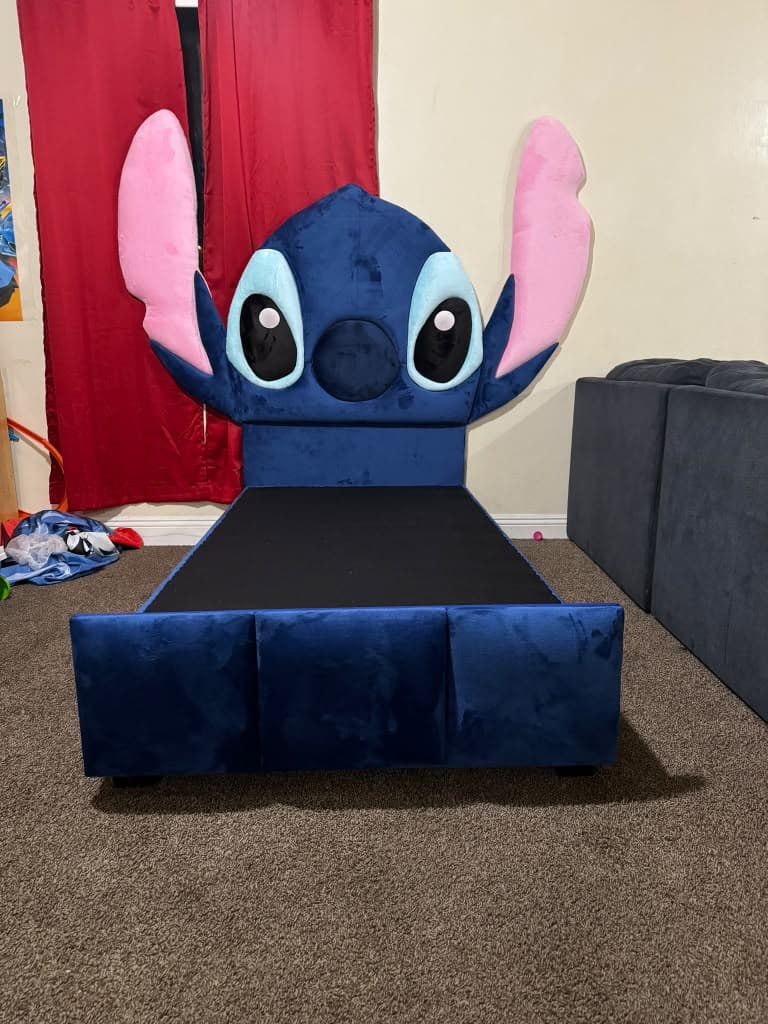 Stitch Bed head-on, an oversized blue velvet headboard sculpted as a character's face with pink ears standing well above the padded footboard
